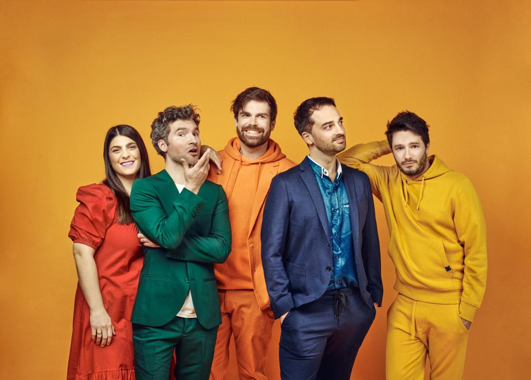 Die fünf Unduzos, darunter eine Frau und vier Männer, befinden sich vor einem gelben Hintergrund und tragen alle Kleidung in unterschiedlichen Farben. Sie schauen fröhlich in verschiedene Richtungen und wirken wie eingeschworenes Team.