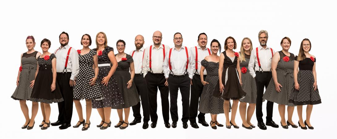 Ein gemischter Chor in loser Reihenfolge mit Damen in Rockabilly Kleidern, die Herren in schwarzen Hosen und weißen Hemden mit roten Hosenträgern